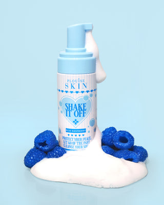 Baby blue bottle of P.Louise Shake It Off Foaming Face Cleanser with foam pouring out of the nozzle surrounded by blue raspberries on a blue background