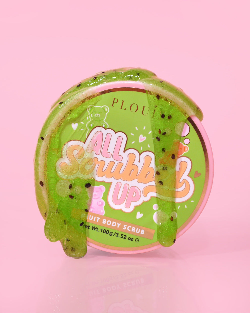 Un contenant de P.Louise All Scrubbed Up Body Scrub portant l'étiquette « Candy Bears » sur fond rose, le produit apparaissant sous la forme d'un gel vert.