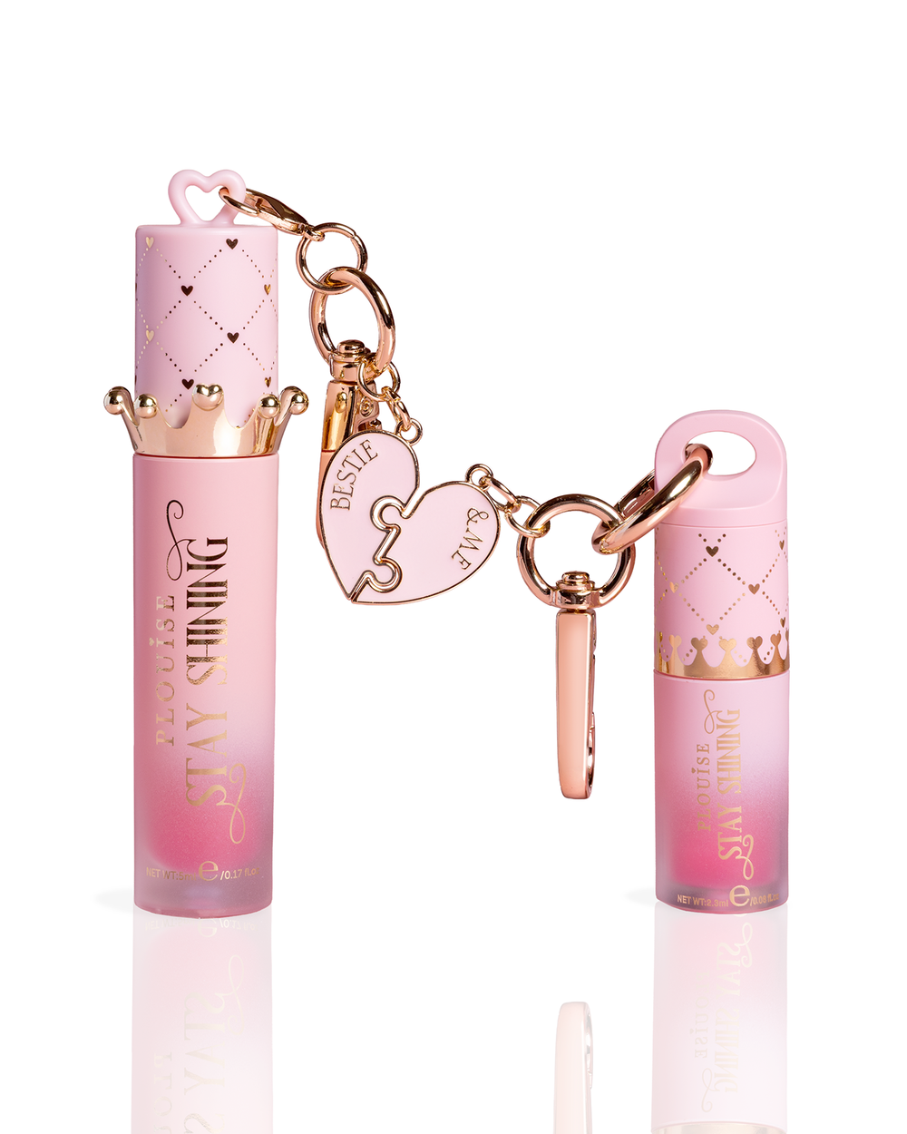 Two pink lip oil tubes with rose gold keychain accessories, including a crown-shaped cap, heart charms, and a keyring, displayed on a clean white background.