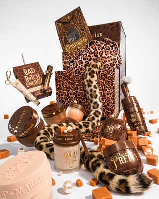 Un coffret cadeau de beauté de luxe orné d'éléments à imprimé marron et léopard, comprenant un sac cadeau à imprimé léopard, une queue à imprimé léopard et plusieurs contenants à cosmétiques dans des tons marron et beige, disposés sur un fond blanc avec des cubes et des perles de couleur caramel.