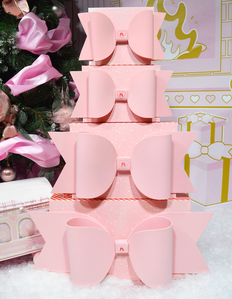 Stapel roze P.Louise-cadeauverpakkingsdozen met strikken tegen een achtergrond met kerstthema en versieringen.