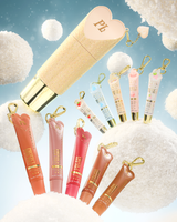 A set of heart-shaped lip conditioner keychain tubes with gold keychains, displayed against a whimsical background of fluffy white clouds and a light blue sky. The set includes a large gold glitter tube with a pink heart cap, several smaller lip gloss or cream tubes in peach, pink, red, and brown shades, and smaller pastel blue and pink keychains.