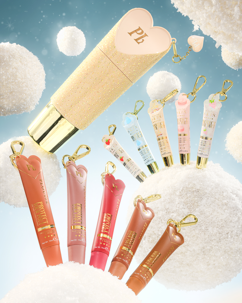 Een set hartvormige sleutelhangerhulzen voor lipconditioners met gouden sleutelhangers, tentoongesteld tegen een grillige achtergrond van pluizige witte wolken en een lichtblauwe lucht. De set bevat een grote gouden glittertube met een roze hartjesdop, verschillende kleinere lipgloss- of crèmetubes in perzik-, roze, rode en bruine tinten, en kleinere pastelblauwe en roze sleutelhangers.