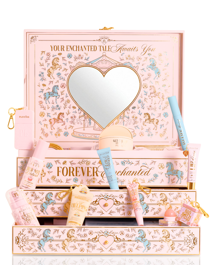A P.Louise pastelroze, blauwe en gele kerst-PR-schoonheidscadeauset met het opschrift 'Your Enchanted Tale' met een hartvormige spiegel op het deksel en open lades, omgeven door diverse cosmetische tubes, flessen en een klein zakje op een witte achtergrond.