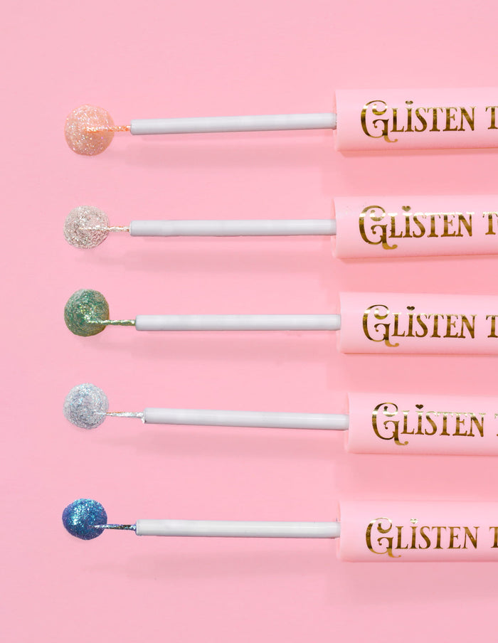 5 eye-liners pailletés P.Louise Glisten To Your Heart alignés avec une goutte de produit au bout sur fond rose