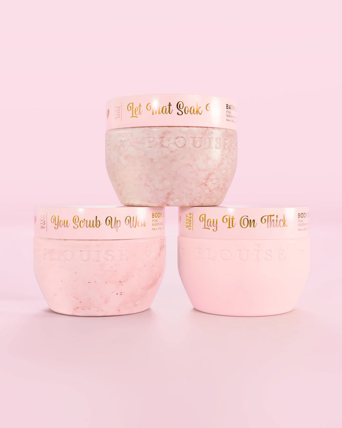 Drie P.Louise Hop Into Self-Care Pink Marshmallow roze containers met badzout, bodyscrub en body butter met gouden tekst op een roze achtergrond