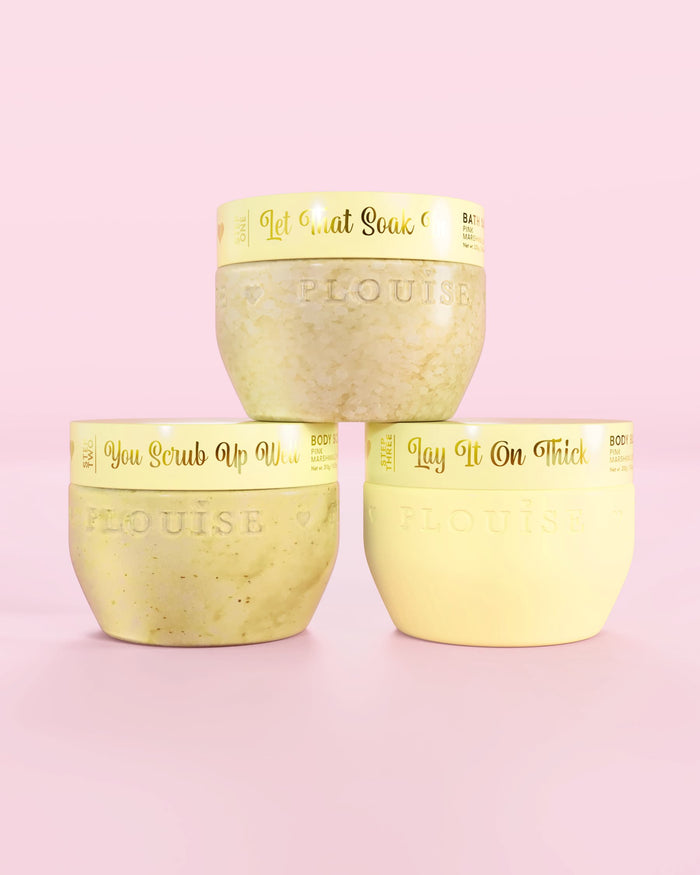 Drie P.Louise Hop Into Self-Care Starwberry Shortcake gele containers met badzout, bodyscrub en body butter met gouden tekst op een roze achtergrond