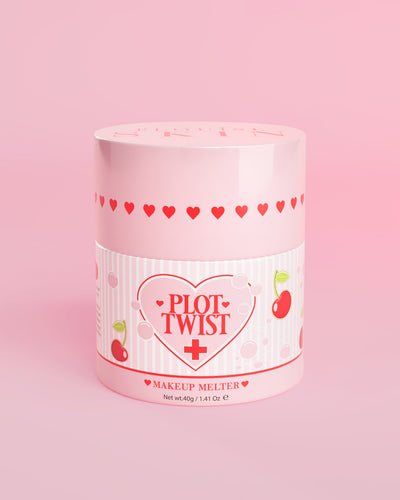 Un contenant rose de baume nettoyant fondant P.Louise Plot Twist Makeup avec des motifs de coeur et de cerise sur l'étiquette sur fond rose