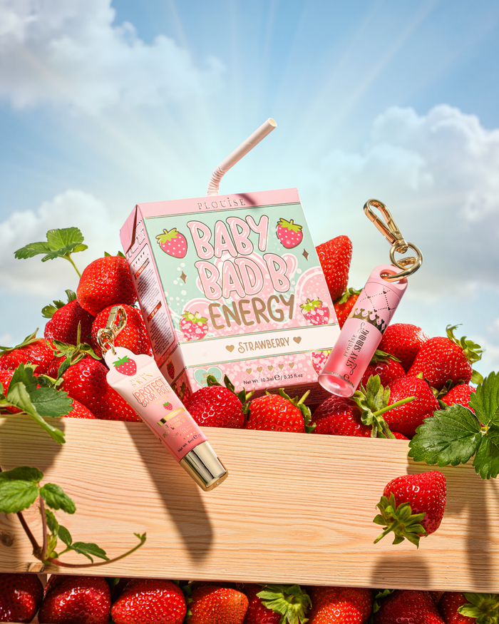 P.Louise Strawberry Baby Bad B Mini Lip Oil en Mini Lip Conditioner op een tafel omringd door aardbeien