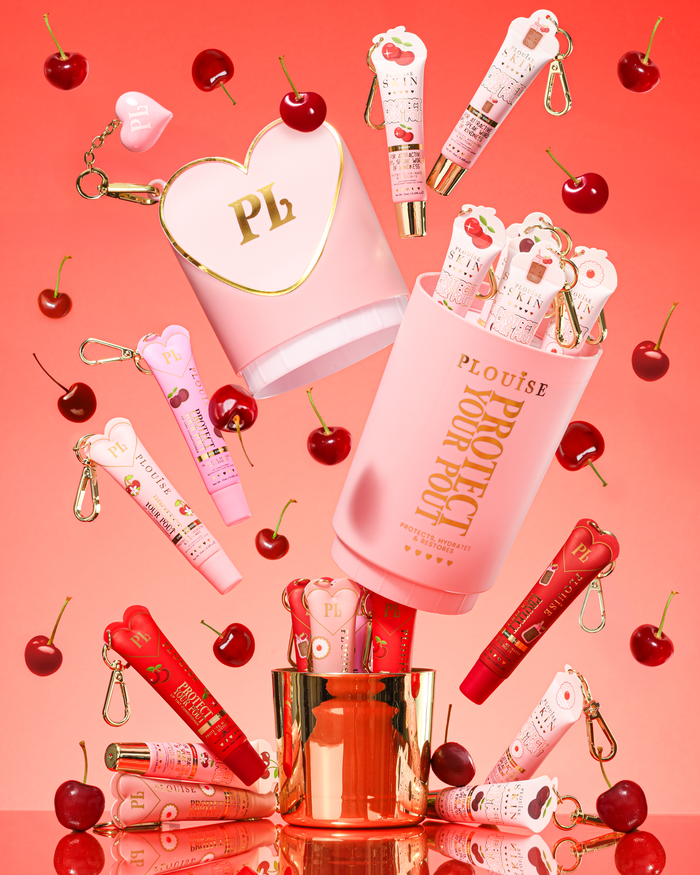 Roze XL Protect Your Pout-cadeauset die is geopend, omringd door kersen en roze en rode lipconditioners op een roze achtergrond