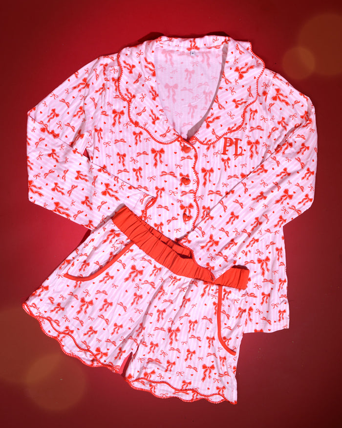 Image d'un pyjama de Noël pour adultes à rayures roses et blanches avec des motifs de nœuds rouges sur fond rouge
