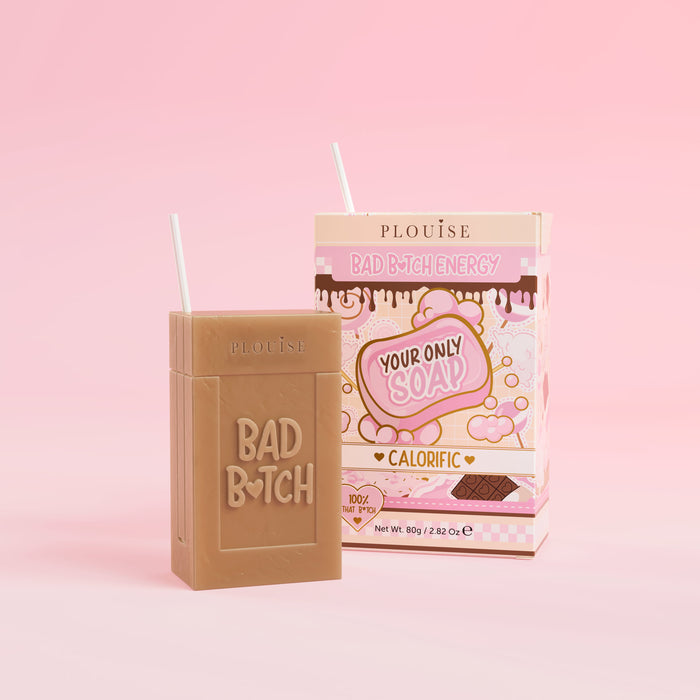 Een bruin stuk zeep met 'Bad Bitch' erop gegraveerd, vergezeld van een kleurrijke sapdoos met het label 'Calorific' erop, gepresenteerd op een roze achtergrond.