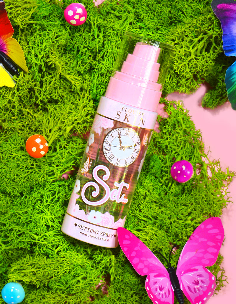 Een fles P. Louise Ready Set Slay Long Lasting Setting Spray omgeven door decoratieve elementen, waaronder kleurrijk nepmos, vlinders en paddenstoelen.