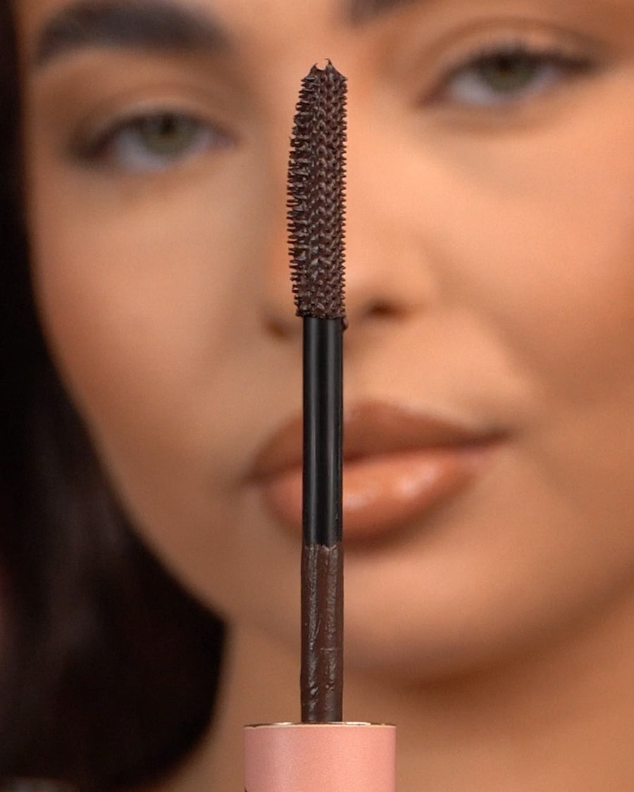 Gros plan d'une baguette de mascara imperméable P.Louise Tearproof tenue devant un visage flou