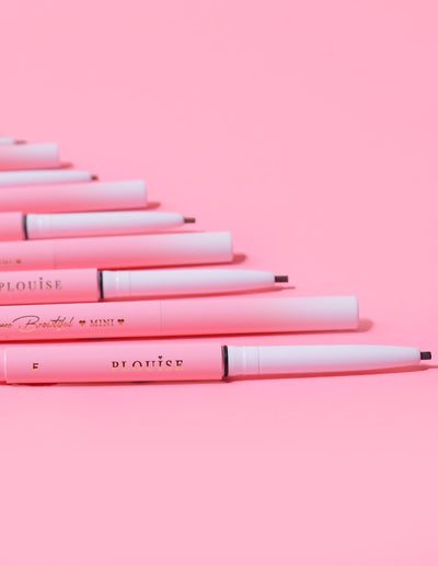 Une collection de mini crayons à sourcils P.Louise disposés en rangée avec le nom de la marque visible sur le corps des crayons, affiché sur fond rose